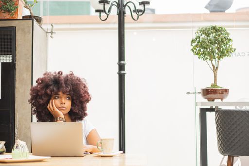 a Young Afro woman in a coffee shop working online at her computer.
