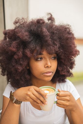 a vertical shot of a young afro woman in a coffee shop enjoying a delicious coffee.