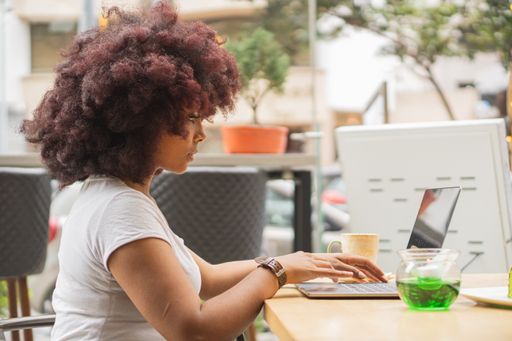 A young African American female in a coffee shop working online at her computer