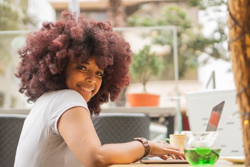 A young African American female in a coffee shop working online at her computer