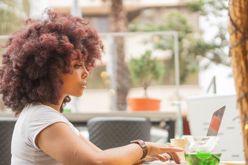 A young African American female in a coffee shop working online at her computer