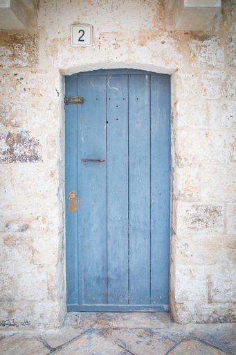 A blue wooden door of an old building and a square signboard with the number 2