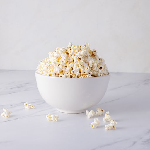 A closeup shot of tasty popcorn in a white bowl on a white surface with a white wall background
