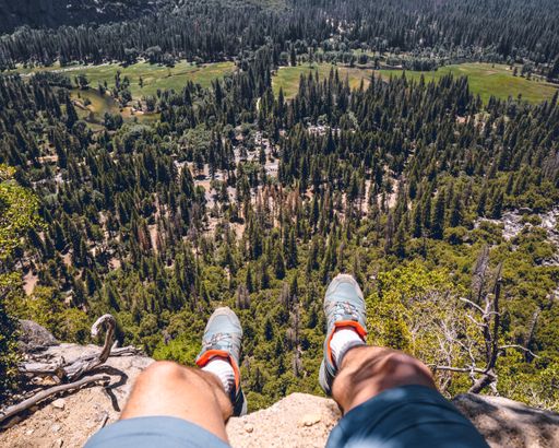 A male's feet hanging at the edge of the cliff overlooking forest trees