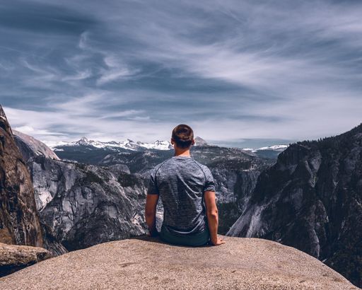 A Caucasian male sitting on the edge of rock cliff while enjoying the beautiful mountain scenery