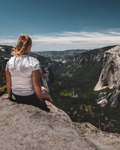 A Caucasian female sitting on the edge of rock cliff while enjoying the beautiful mountain scenery