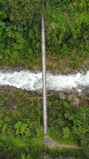 A vertical drone shot of a hanging bridge over a river.