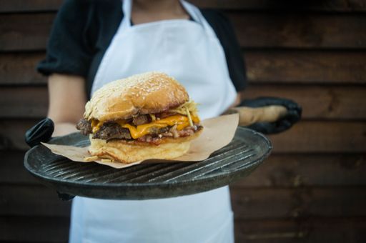 A close-up shot of a chef holding a burger on a black ceramic plate.