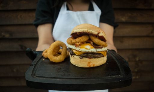 A close-up shot of a chef holding a burger and onion rings on a black painted wooden plate.