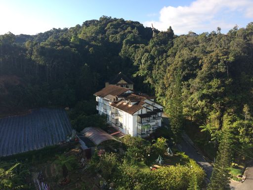 An aerial shot of a brown and white house surrounded by green trees in a forest on hills