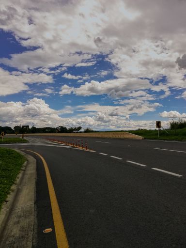 An empty asphalt road with sharp curve signs on blue cloudy sky