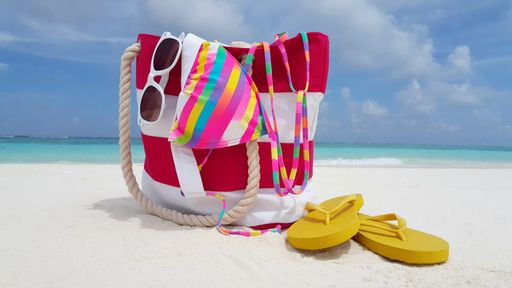 A closeup of a female bag and flip-flops on a sandy beach