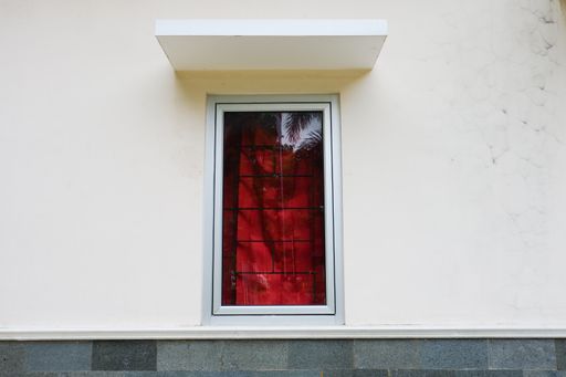 An outside shot of a window with red curtain and a lattice behind