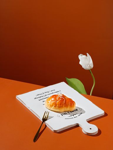 A vertical shot of croissants on white board near a white tulip flower