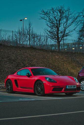 A vertical shot of candy red Porsche 718 parked in an outdoor car park in Basingstoke, UK