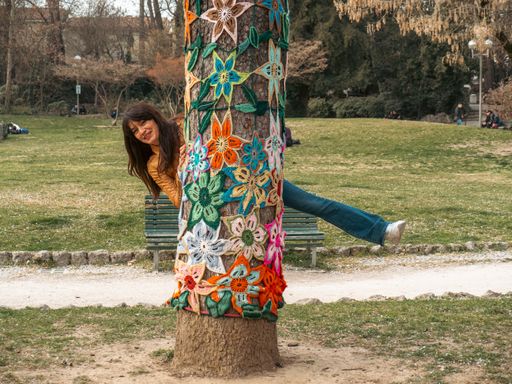 A beautiful shot of a Hispanic pretty woman hugging and looking behind a tree in the garden
