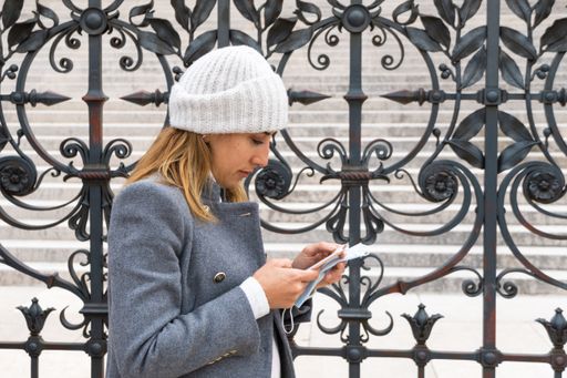 A closeup shot of a Caucasian young woman wearing a white hat checking her mobile phone next to metal gate