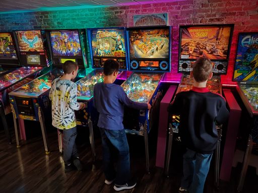 A boys play pinball machines in an entertainment center with colorful lighting
