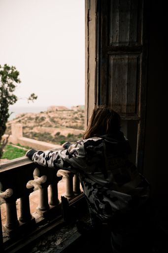 A vertical shot of a woman with long hair looks out the window