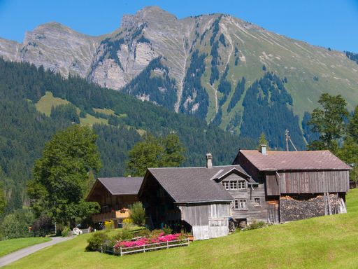 a shot of small houses on hill against green mountain peaks