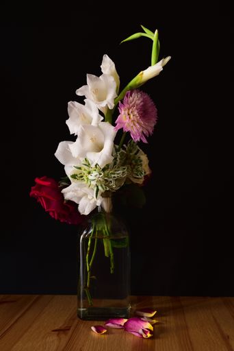 A vertical shot of different flowers in a jar on a wooden surface with a black background