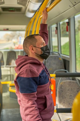 A Hispanic male standing inside the modern bus wearing a black face mask on a sunny day