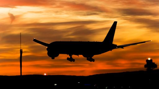 A silhouette of an airplane landing at the airport in the sunset.