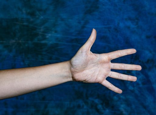 A horizontal closeup shot of a hand showing number five or an open palm on a marbled blue background