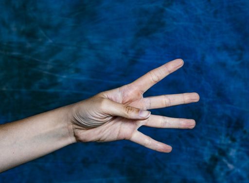 A horizontal closeup shot of a hand showing number four on a marbled blue background
