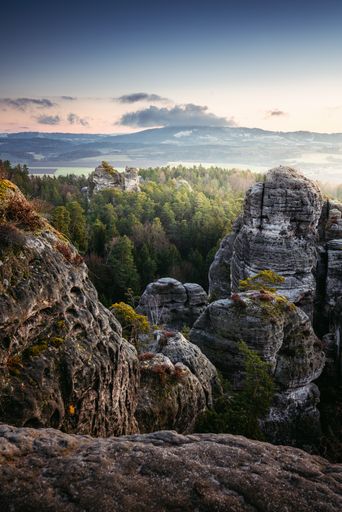 A landscape view of sandstone rocks and trees under a cloudy sky in Bohemian or Czech Paradise national park