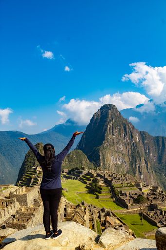 A vertical shot of a Caucasian woman looking at Machu Picchu's ancient city.