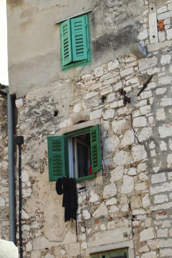 A vertical shot of an old stone house with windows with green shutters during daylight