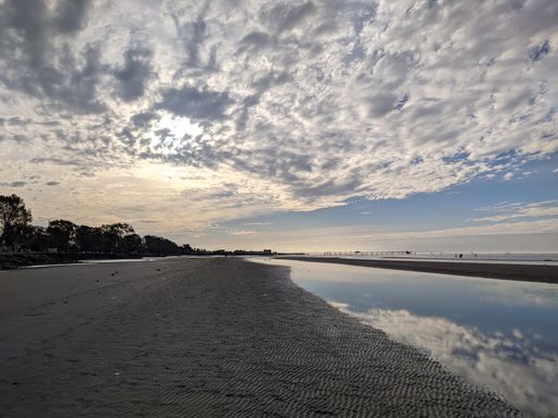 The cloudy blue sky over the calm coast and sandy beach in summer