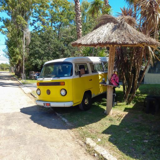 old classic yellow Volkswagen Type 2 T2 Camper Kombi van camping beside a straw parasol. Green trees nature background. Suda VW classic cars Copyspace