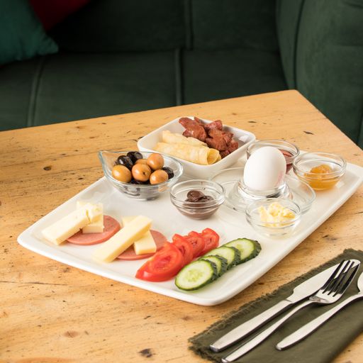 A white plate with cucumbers, tomatoes, sausage, eggs, olives, and sauce on a wooden table
