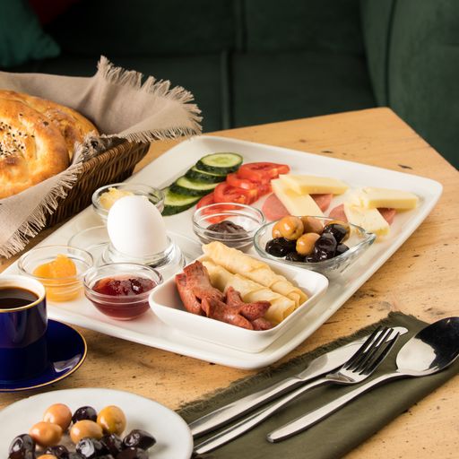 A white plate with cucumbers, tomatoes, sausage, eggs, olives, and sauce on a wooden table