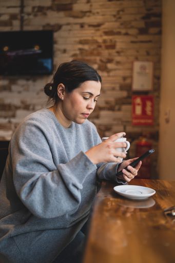 A vertical shot of a Caucasian woman drinking coffee and checking her phone in a cafe