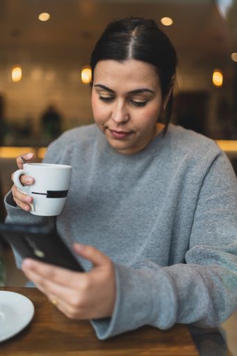 A vertical shot of a Caucasian woman drinking coffee and checking her phone in a cafe