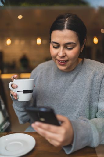 A vertical shot of a Caucasian woman drinking coffee and checking her phone in a cafe