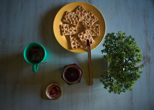 A high angle view of crackers on a plate on the table with a cup of tea and jam under the lights