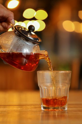 A vertical shot of a person pouring tea into a glass from a teapot
