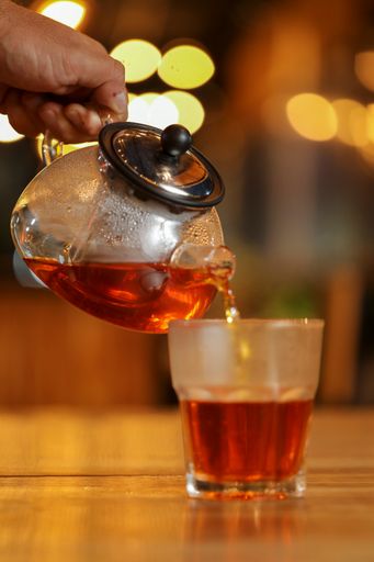 A vertical shot of a person pouring tea into a glass from a teapot