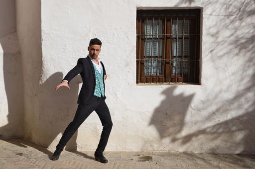 A young man dressed in black and wearing red shoes dancing flamenco on a street, Seville, Spain