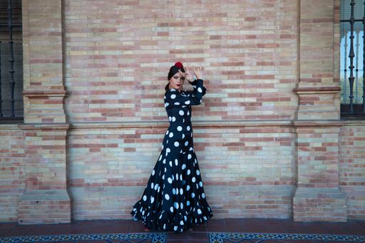 A Hispanic brunette flamenco dancer wearing a white polka dots dress against brown brick wall in Seville