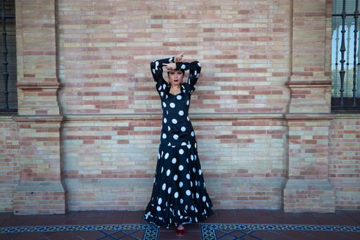 A Hispanic brunette flamenco dancer wearing a white polka dots dress against brown brick wall in Seville