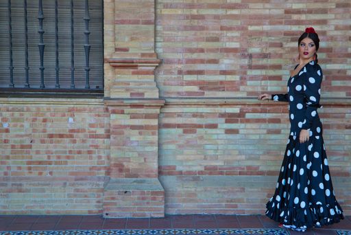A Hispanic brunette flamenco dancer wearing a white polka dots dress against brown brick wall in Seville