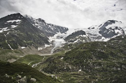 A view of a narrow road surrounded by tall mountains covered with snow on top