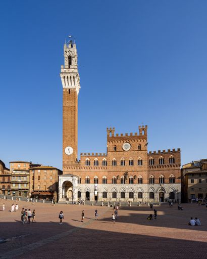 The Tower of Mangia (Torre del Mangia), against blue sky in bright sunlight in Campo Square (Piazza del Campo) in Siena, Tuscany, Italy