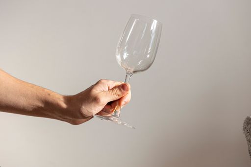 A closeup shot of a glass cup in a man's hand against gray wall
