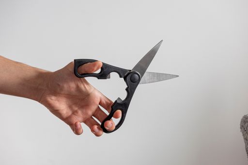 A closeup shot of a man's arm holding black scissors against white wall